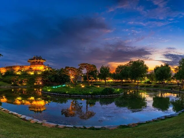 Ein traditioneller koreanischer Pavillon, der nachts beleuchtet wird und sich in einem ruhigen Teich spiegelt.