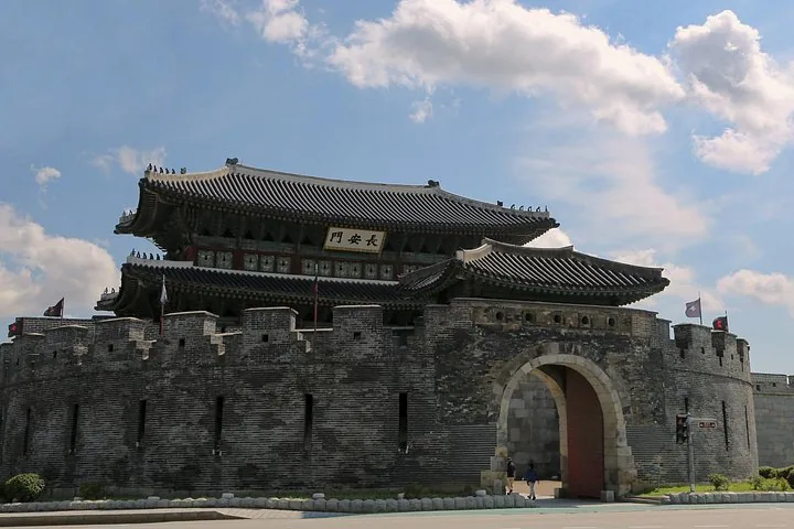 Un gran edificio tradicional de puerta coreana en lo alto de un muro de piedra curvo de la fortaleza.