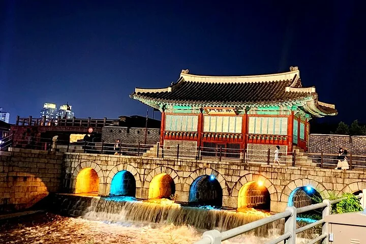 Una struttura a padiglione tradizionale coreana su un ponte di pietra con luci colorate.