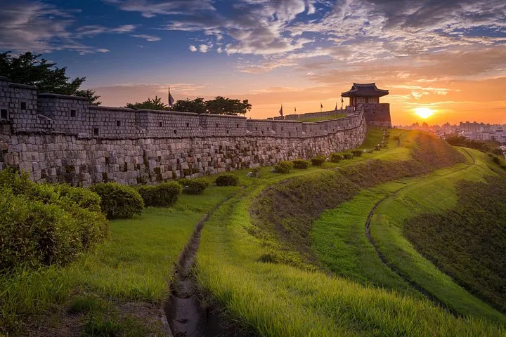 Tramonto su una lunga muraglia in pietra con una tradizionale struttura a padiglione.