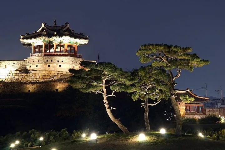Un pavillon traditionnel coréen illuminé sur le mur d'une forteresse la nuit avec des pins.