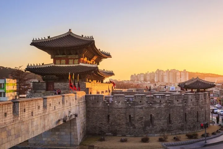 A large traditional Korean gate structure on a stone wall at sunset.