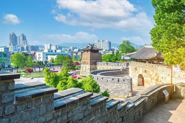 A traditional Korean pavilion on a fortress wall overlooking a modern city skyline.